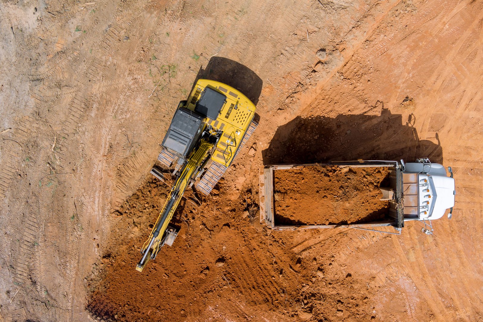 Excavator operator is carefully positioning scoop on soil is into dumper truck